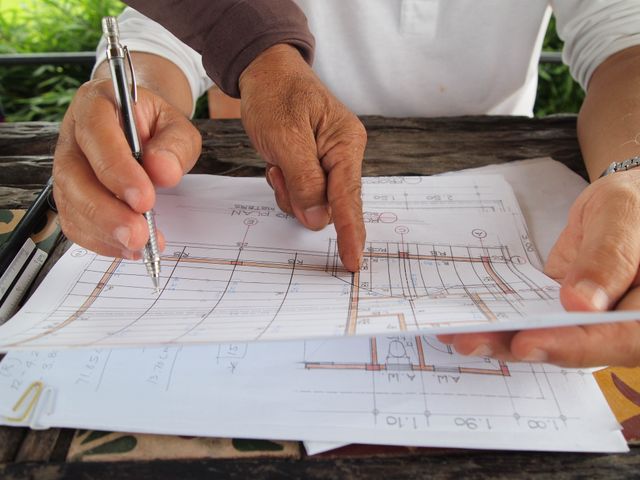 Two architects reviewing and discussing detailed blueprints at a workspace.